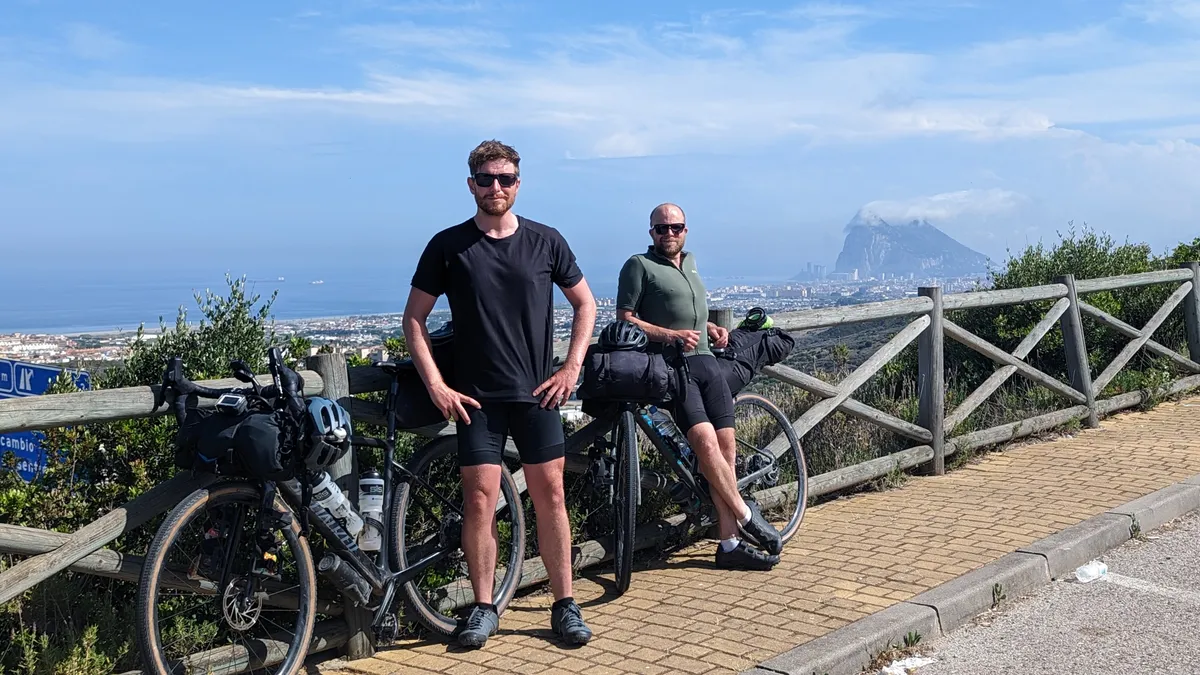 The brothers with loaded bikepacking bikes at a roadside viewpoint, the Rock of Gibraltar on the horizon