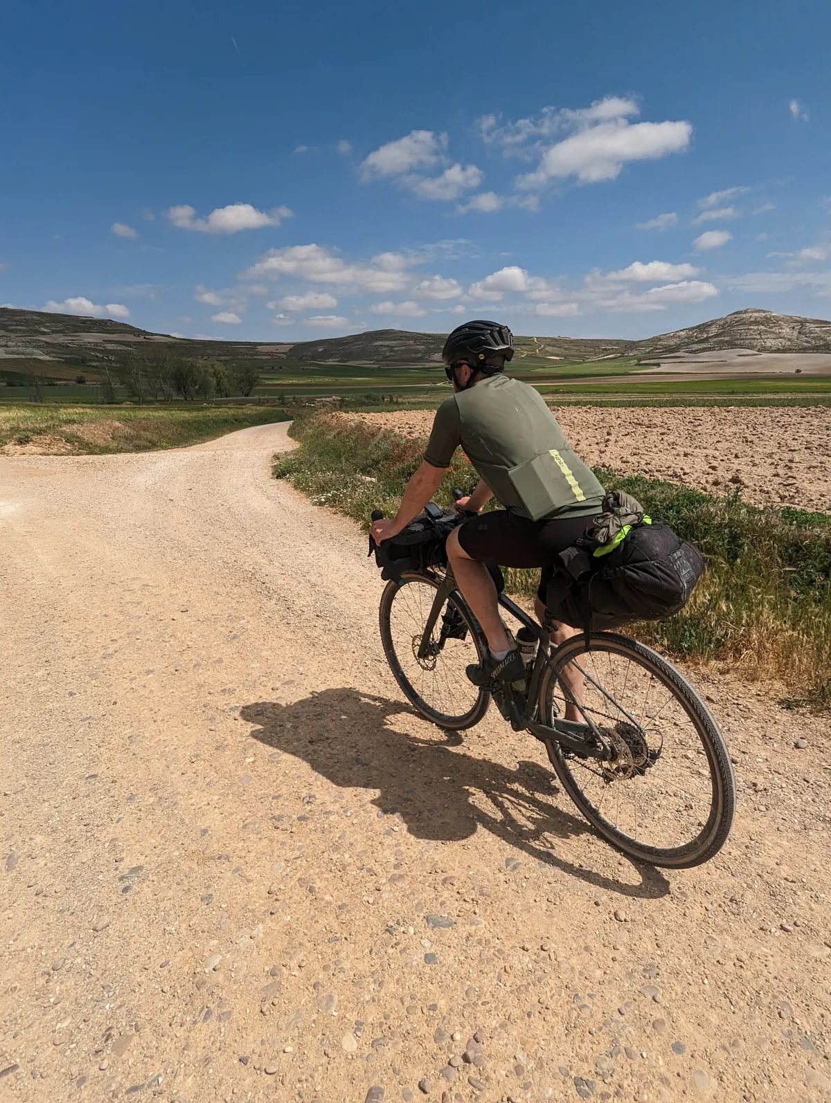 One brother riding a loaded gravel bike along a dusty white gravel road through open Spanish farmland