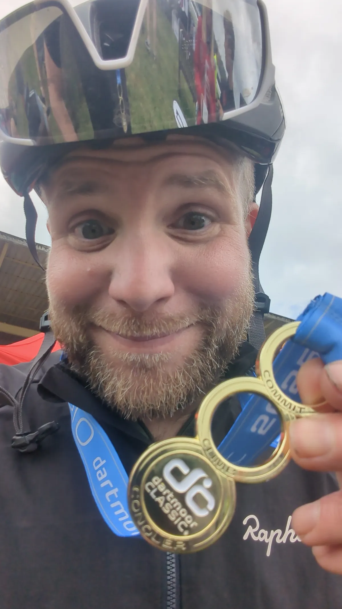Grinning close-up selfie holding up the interlocking gold Dartmoor Classic finisher medals
