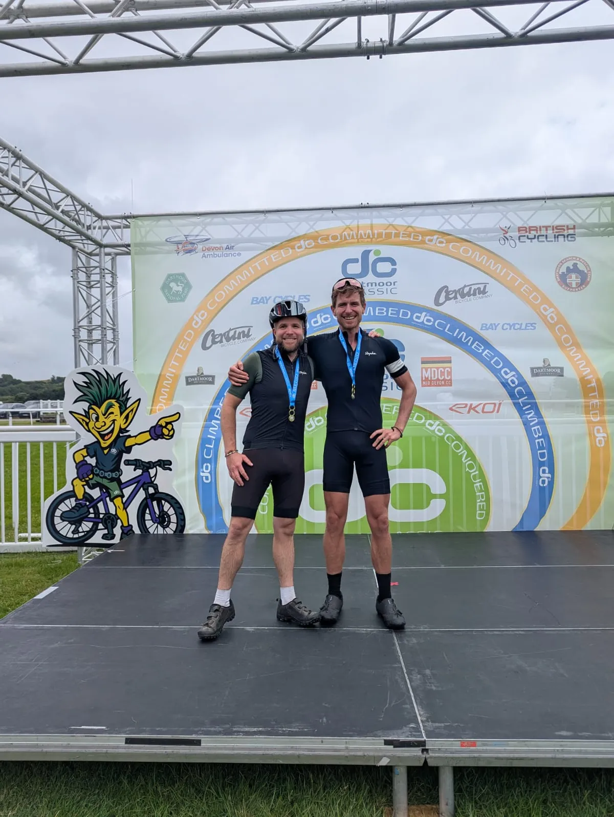 The two Cycle Bros brothers on the Dartmoor Classic podium stage, arms round each other, finisher medals on