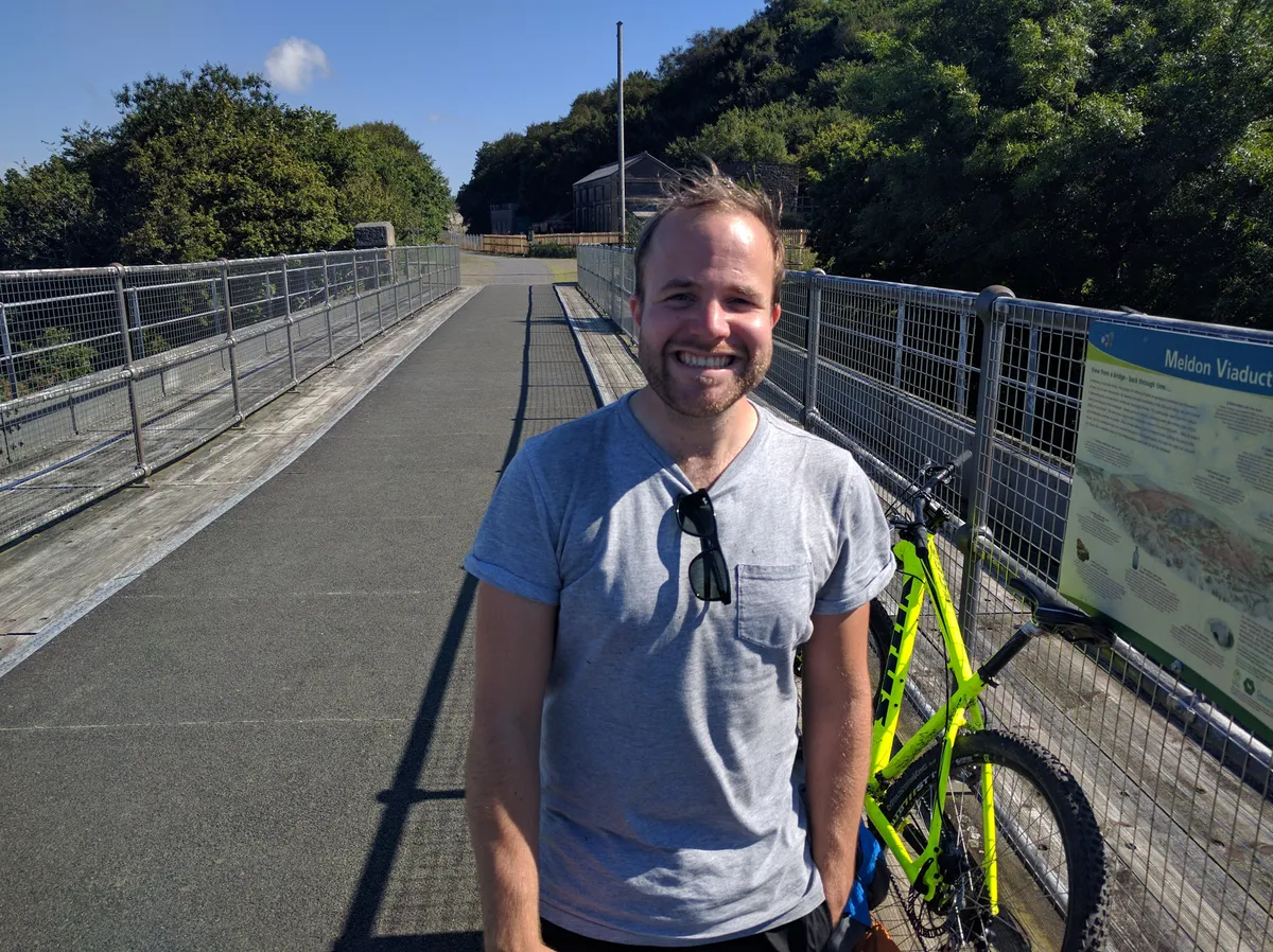 A younger brother grinning on Meldon Viaduct with a yellow hybrid bike propped on the railings