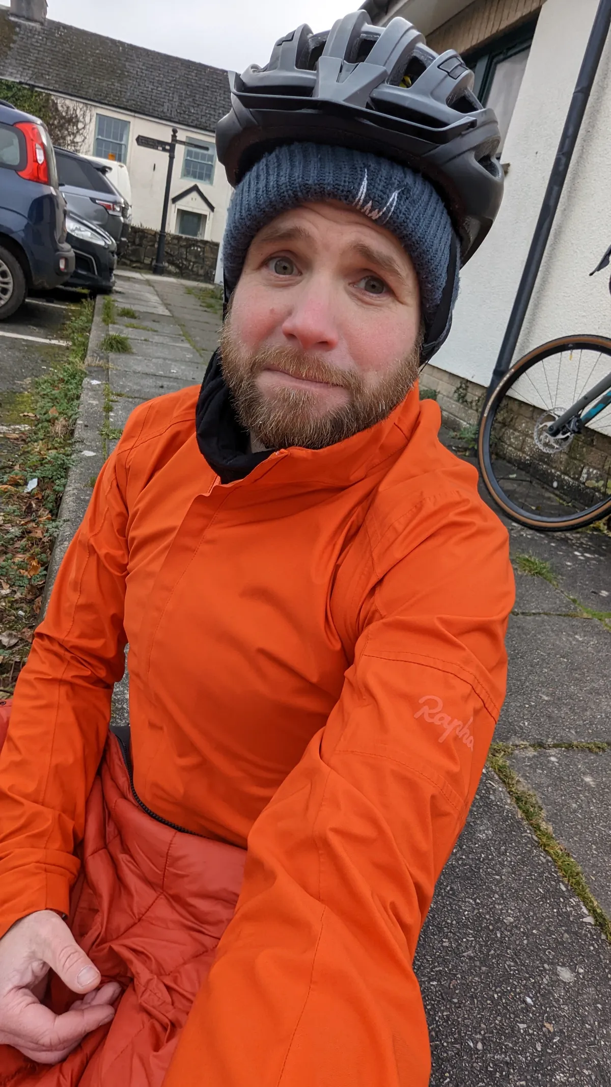 Cold, rosy-cheeked selfie in an orange rain jacket and woolly hat under a helmet